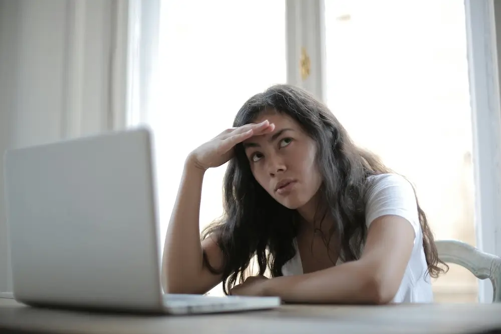 Young woman sitting in front of a laptop, clearly confused by what she is seeing